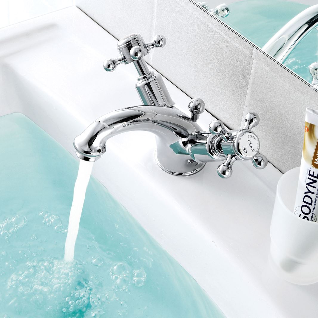 Crosshead lever basin mixer tap with pop up waste installed on a basin showing water flowing from the tap into the basin