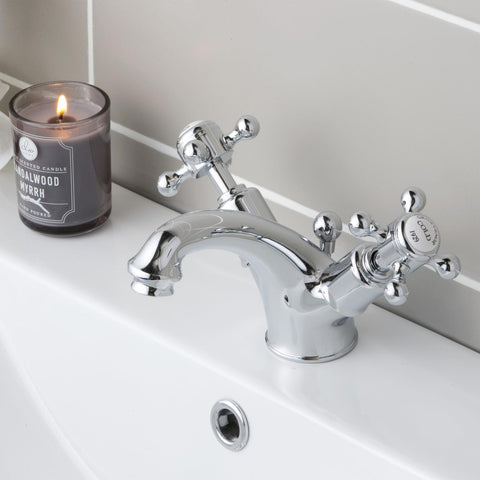 Two handles crosshead  basin mixer tap installed on a basin with a burning candle next to it